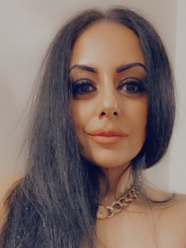 Sukhvinder Javeed, with long dark hair and a gold chain, looking straight at the camera